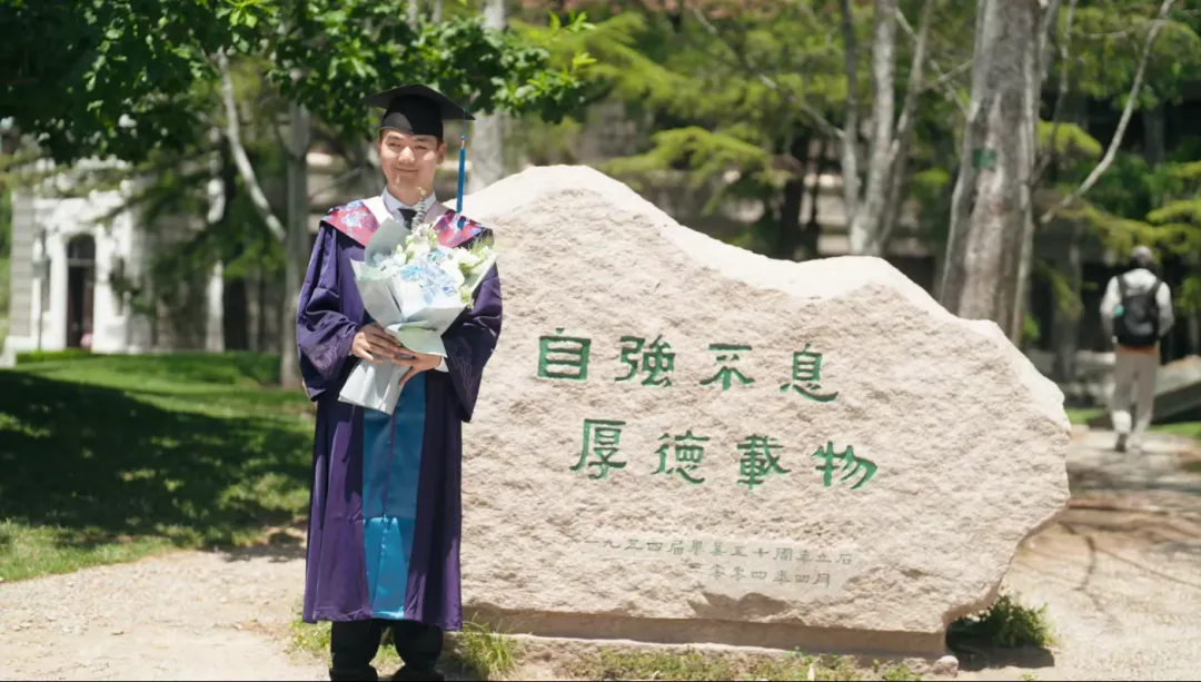 梁江波身穿硕士服，站在镌刻着“自强不息，厚德载物”的清华大学校训石前留影.png